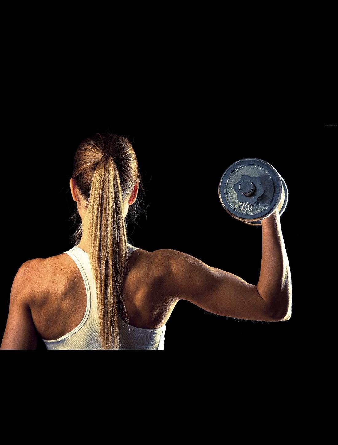 A woman pressing a dumbbell overhead, shot from behind