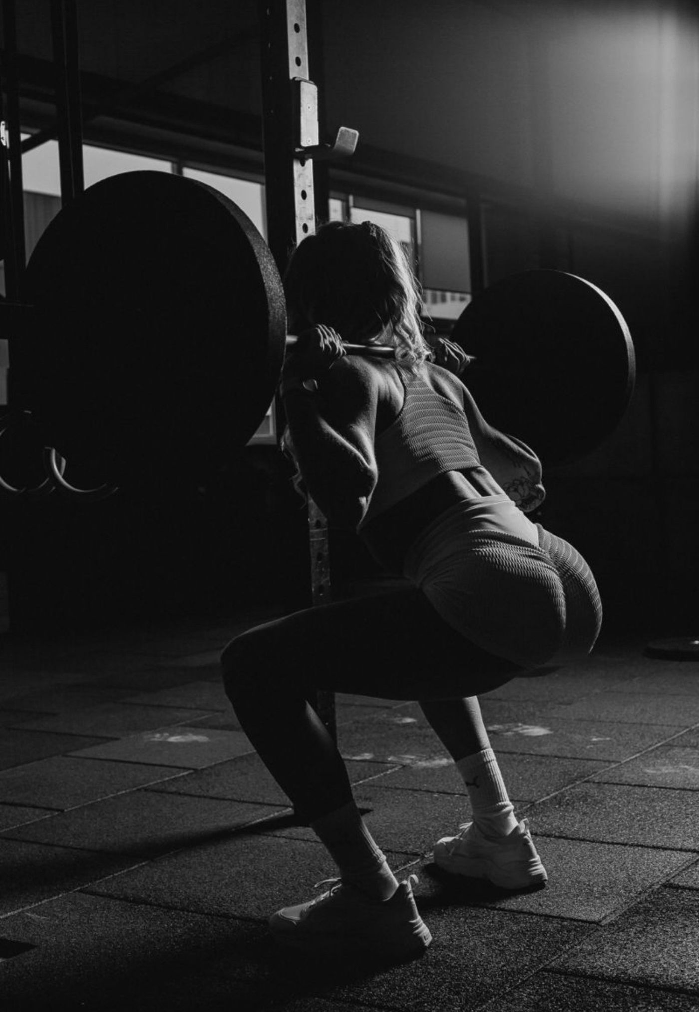 A woman squatting under a loaded barbell in a dark gym